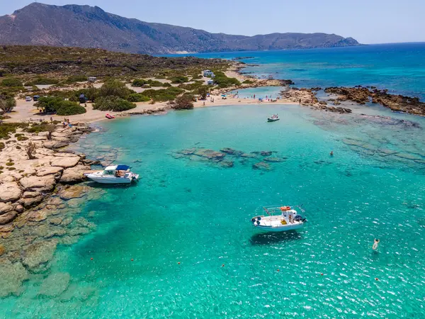 Elafonissi Sahili 'nin nefes kesici hava manzarası kristal berrak turkuaz sularını ve yumuşak pembe kumunu sergiliyor. Durgun denizde beyaz kayıklar süzülüyor, sakin kıyı manzarasına yeni bir renk katıyor.