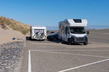 Bir araba ve bir karavan Hollanda 'nın Zeeland plajı yakınlarında park edilmiş. İki bisiklet güvenli bir şekilde araca bağlı, manzaralı kıyı manzarası boyunca bir maceraya hazır..