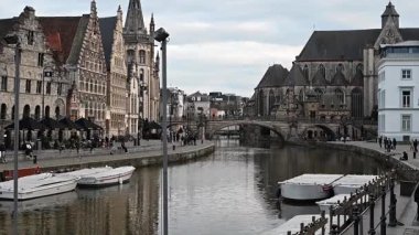 Gent, Belçika - 23 Mart 2025: Gent, Belçika 'da, büyüleyici tarihi mimari ve sudaki yansımalarla çevrili, kanallar boyunca yürüyen insanları gösteren resimli bir video. Canlı ve büyüleyici bir şehir..