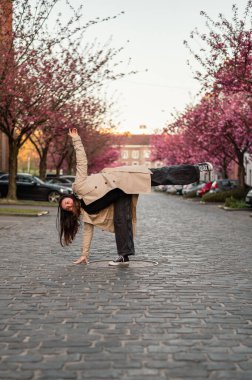Belçika, Gent 'te bir kaldırım taşı caddesinde çiçek açan kiraz ağaçlarının altında bej ceketli bir kadının büyüleyici bir sahnesi. Yumuşak pembe yapraklar rüya gibi bir bahar havası yaratır..
