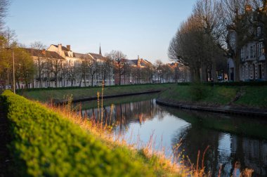 Gün doğumunda Gent 'te sakin bir kanal manzarası. Yumuşak sabah ışığı sakin suyu yansıtıyor, tarihi mimariyi vurguluyor ve barışçıl, resimsel bir atmosfer yaratıyor..