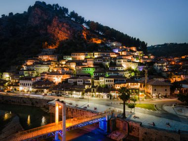 Osum Nehri üzerindeki Berat kasabasında gün batımı, beyaz Osmanlı evleriyle tanınıyor. Ayrıca Bin Pencere Şehri olarak da bilinir. Kalenin altındaki yamaca karşı inşa edilmiştir..