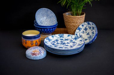 Güzel desenli mavi ve beyaz porselen kaseler ve tabaklar, bir saksı bitkisi ve dekoratif bir mum eşliğinde, rafine bir sofra takımı oluşturur.