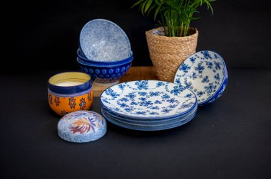Güzel desenli mavi ve beyaz porselen kaseler ve tabaklar, bir saksı bitkisi ve dekoratif bir mum eşliğinde, rafine bir sofra takımı oluşturur.