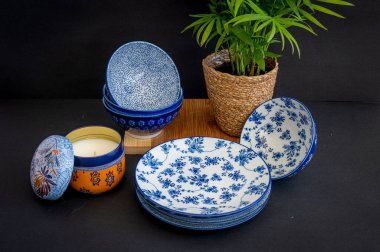 Güzel desenli mavi ve beyaz porselen kaseler ve tabaklar, bir saksı bitkisi ve dekoratif bir mum eşliğinde, rafine bir sofra takımı oluşturur.