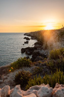 Maltas 'ın nefes kesici manzarası engebeli taştan kıyı şeridi ılık günbatımı renkleriyle yıkanmış, kayalardan yansıyan altın ışık ve sakin Akdeniz.
