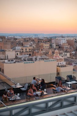 Valletta, Malta - 22 Temmuz 2022: Günbatımında Valletta çatılarının çarpıcı hava manzarası, insanların akşam içkilerinin keyfini çıkardığı. Şehrin tarihi kubbeleri ve kireçtaşı binaları parlıyor.