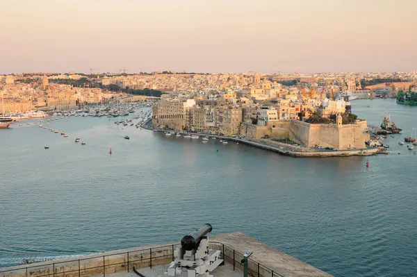 Birgu Limanı 'nın çarpıcı panoramik manzarası Valletta bakış açısından, tarihi mimari, kenetlenmiş tekneler ve manzaralı Malta kıyı şeridi sergileniyor..