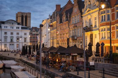 Gent, Belçika - 23 Mart 2025: Belçika 'nın Gent kentinin muhteşem tarihi mimarisi ve su üzerindeki yansımaları ile çevrili, kanallar boyunca yürüyen insanları gösteren fotografik bir çekimi.