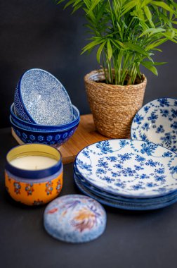 Güzel desenli mavi ve beyaz porselen kaseler ve tabaklar, bir saksı bitkisi ve dekoratif bir mum eşliğinde, rafine bir sofra takımı oluşturur.