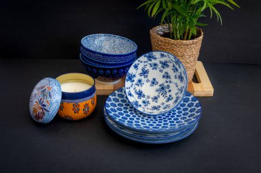 Güzel desenli mavi ve beyaz porselen kaseler ve tabaklar, bir saksı bitkisi ve dekoratif bir mum eşliğinde, rafine bir sofra takımı oluşturur.