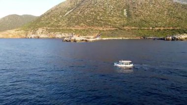 Yunanistan 'ın Girit kentindeki Bali Körfezi' nin berrak sularında yavaşça yüzen küçük bir tekne. Kayalık tepeler ve turkuaz denizlerle çevrili sakin kıyı manzarası huzurlu ve pitoresk bir manzara yaratır..