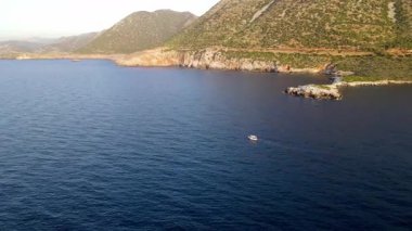 Yunanistan 'ın Girit kentindeki Bali Körfezi' nin berrak sularında yavaşça yüzen küçük bir tekne. Kayalık tepeler ve turkuaz denizlerle çevrili sakin kıyı manzarası huzurlu ve pitoresk bir manzara yaratır..