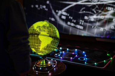 Etkileşimli mavi bir küre ve dijital verileri gösteren fütüristik bir ekranın yer aldığı atmosferik bir sahne. Bir insan dünyayı modern teknolojiyle keşfeder, neon ışıklarla aydınlatılır.