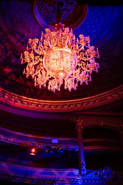 Bir tiyatroda asılı muhteşem bir avize zarif tasarımı ve sıcak altın parıltısıyla dekoratif iç mekanı aydınlatıyor..