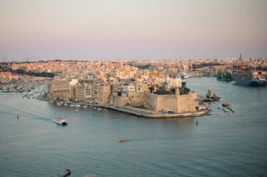 Birgu Limanı 'nın çarpıcı panoramik manzarası Valletta bakış açısından, tarihi mimari, kenetlenmiş tekneler ve manzaralı Malta kıyı şeridi sergileniyor..