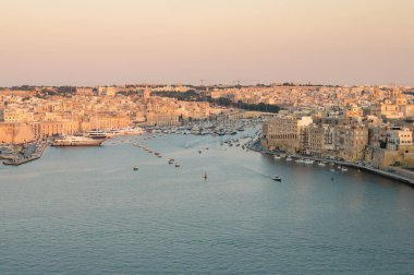 Birgu Limanı 'nın çarpıcı panoramik manzarası Valletta bakış açısından, tarihi mimari, kenetlenmiş tekneler ve manzaralı Malta kıyı şeridi sergileniyor..