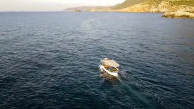 Yunanistan 'ın Girit kentindeki Bali Körfezi' nin berrak sularında yavaşça yüzen küçük bir tekne. Kayalık tepeler ve turkuaz denizlerle çevrili sakin kıyı manzarası huzurlu ve pitoresk bir manzara yaratır..