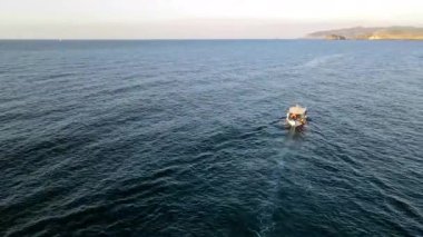 Yunanistan 'ın Girit kentindeki Bali Körfezi' nin berrak sularında yavaşça yüzen küçük bir tekne. Kayalık tepeler ve turkuaz denizlerle çevrili sakin kıyı manzarası huzurlu ve pitoresk bir manzara yaratır..