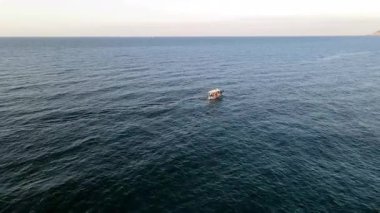 Yunanistan 'ın Girit kentindeki Bali Körfezi' nin berrak sularında yavaşça yüzen küçük bir tekne. Kayalık tepeler ve turkuaz denizlerle çevrili sakin kıyı manzarası huzurlu ve pitoresk bir manzara yaratır..