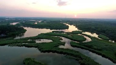 Gün batımında Ukrayna kırsalında yerleşmiş huzurlu bir nehir kenarı tatil köyünün nefes kesici hava manzarası. Altın ışık suyu yansıtır, dingin ve görkemli bir manzara yaratır..