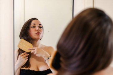 Bir kadın, günlük güzellik hizmetinin bir parçası olarak saçlarını nazikçe tarar. Sağlıklı, pürüzsüz ve bakımlı kilitleri teşvik eder..