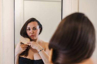 Bir kadın, günlük güzellik hizmetinin bir parçası olarak saçlarını nazikçe tarar. Sağlıklı, pürüzsüz ve bakımlı kilitleri teşvik eder..