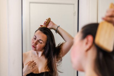 Bir kadın, günlük güzellik hizmetinin bir parçası olarak saçlarını nazikçe tarar. Sağlıklı, pürüzsüz ve bakımlı kilitleri teşvik eder..