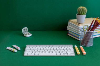 Yeşil bir arkaplanda düzenli olarak dizilmiş not defterleri, kalemler, keçeli kalemler ve makaslar da dahil olmak üzere okul malzemelerinden oluşan canlı bir çeşitlilik.