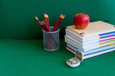 Yeşil bir arkaplanda düzenli olarak dizilmiş not defterleri, kalemler, keçeli kalemler ve makaslar da dahil olmak üzere okul malzemelerinden oluşan canlı bir çeşitlilik.