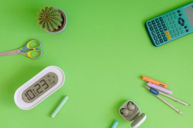 Yeşil bir arkaplanda düzenli olarak dizilmiş not defterleri, kalemler, keçeli kalemler ve makaslar da dahil olmak üzere okul malzemelerinden oluşan canlı bir çeşitlilik.