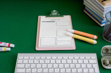 Yeşil bir arkaplanda düzenli olarak dizilmiş not defterleri, kalemler, keçeli kalemler ve makaslar da dahil olmak üzere okul malzemelerinden oluşan canlı bir çeşitlilik.