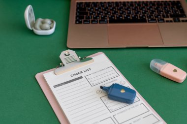 Yeşil bir arkaplanda düzenli olarak dizilmiş not defterleri, kalemler, keçeli kalemler ve makaslar da dahil olmak üzere okul malzemelerinden oluşan canlı bir çeşitlilik.