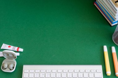 Yeşil bir arkaplanda düzenli olarak dizilmiş not defterleri, kalemler, keçeli kalemler ve makaslar da dahil olmak üzere okul malzemelerinden oluşan canlı bir çeşitlilik.