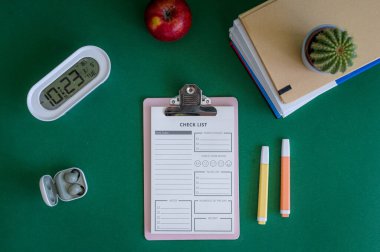 Yeşil bir arkaplanda düzenli olarak dizilmiş not defterleri, kalemler, keçeli kalemler ve makaslar da dahil olmak üzere okul malzemelerinden oluşan canlı bir çeşitlilik.