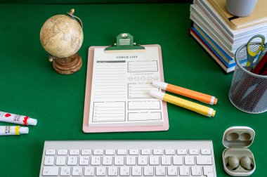 Yeşil bir arkaplanda düzenli olarak dizilmiş not defterleri, kalemler, keçeli kalemler ve makaslar da dahil olmak üzere okul malzemelerinden oluşan canlı bir çeşitlilik.