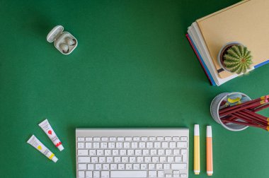 Yeşil bir arkaplanda düzenli olarak dizilmiş not defterleri, kalemler, keçeli kalemler ve makaslar da dahil olmak üzere okul malzemelerinden oluşan canlı bir çeşitlilik.