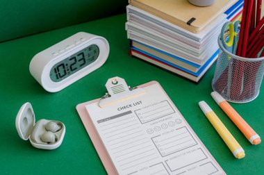 Yeşil bir arkaplanda düzenli olarak dizilmiş not defterleri, kalemler, keçeli kalemler ve makaslar da dahil olmak üzere okul malzemelerinden oluşan canlı bir çeşitlilik.