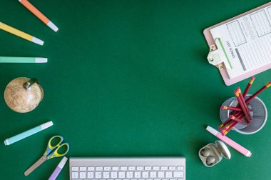 Yeşil bir arkaplanda düzenli olarak dizilmiş not defterleri, kalemler, keçeli kalemler ve makaslar da dahil olmak üzere okul malzemelerinden oluşan canlı bir çeşitlilik.