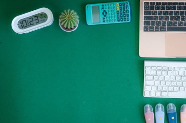 Yeşil bir arkaplanda düzenli olarak dizilmiş not defterleri, kalemler, keçeli kalemler ve makaslar da dahil olmak üzere okul malzemelerinden oluşan canlı bir çeşitlilik.