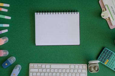 Yeşil bir arkaplanda düzenli olarak dizilmiş not defterleri, kalemler, keçeli kalemler ve makaslar da dahil olmak üzere okul malzemelerinden oluşan canlı bir çeşitlilik.