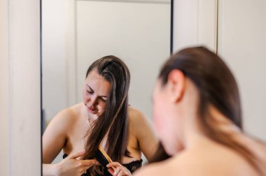 Bir kadın, günlük güzellik hizmetinin bir parçası olarak saçlarını nazikçe tarar. Sağlıklı, pürüzsüz ve bakımlı kilitleri teşvik eder..