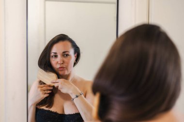 Bir kadın, günlük güzellik hizmetinin bir parçası olarak saçlarını nazikçe tarar. Sağlıklı, pürüzsüz ve bakımlı kilitleri teşvik eder..