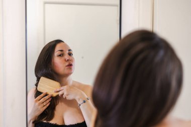 Bir kadın, günlük güzellik hizmetinin bir parçası olarak saçlarını nazikçe tarar. Sağlıklı, pürüzsüz ve bakımlı kilitleri teşvik eder..