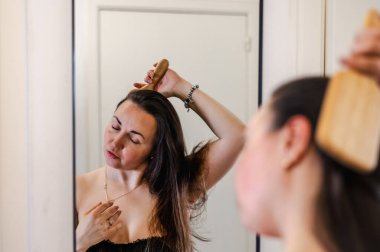 Bir kadın, günlük güzellik hizmetinin bir parçası olarak saçlarını nazikçe tarar. Sağlıklı, pürüzsüz ve bakımlı kilitleri teşvik eder..