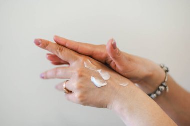 Hafif manikürlü, nemlendirici krem süren zarif kadın ellerinin yakın çekimi. Nazik el bakımı ve güzellik tedavisi.