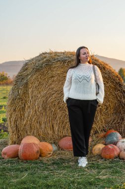 Sade beyaz kazaklı bir kadın sonbahar hasat mevsiminde renkli balkabakları ve süs kabaklarıyla dolu bir çiftlik pazarını keşfediyor..
