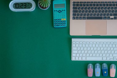 Yeşil bir arkaplanda düzenli olarak dizilmiş not defterleri, kalemler, keçeli kalemler ve makaslar da dahil olmak üzere okul malzemelerinden oluşan canlı bir çeşitlilik.