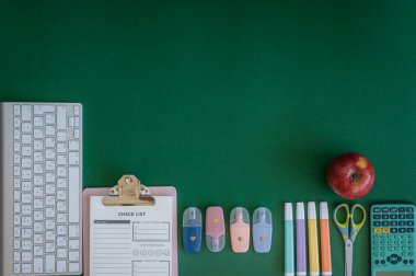 Yeşil bir arkaplanda düzenli olarak dizilmiş not defterleri, kalemler, keçeli kalemler ve makaslar da dahil olmak üzere okul malzemelerinden oluşan canlı bir çeşitlilik.
