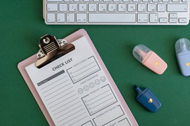 Yeşil bir arkaplanda düzenli olarak dizilmiş not defterleri, kalemler, keçeli kalemler ve makaslar da dahil olmak üzere okul malzemelerinden oluşan canlı bir çeşitlilik.